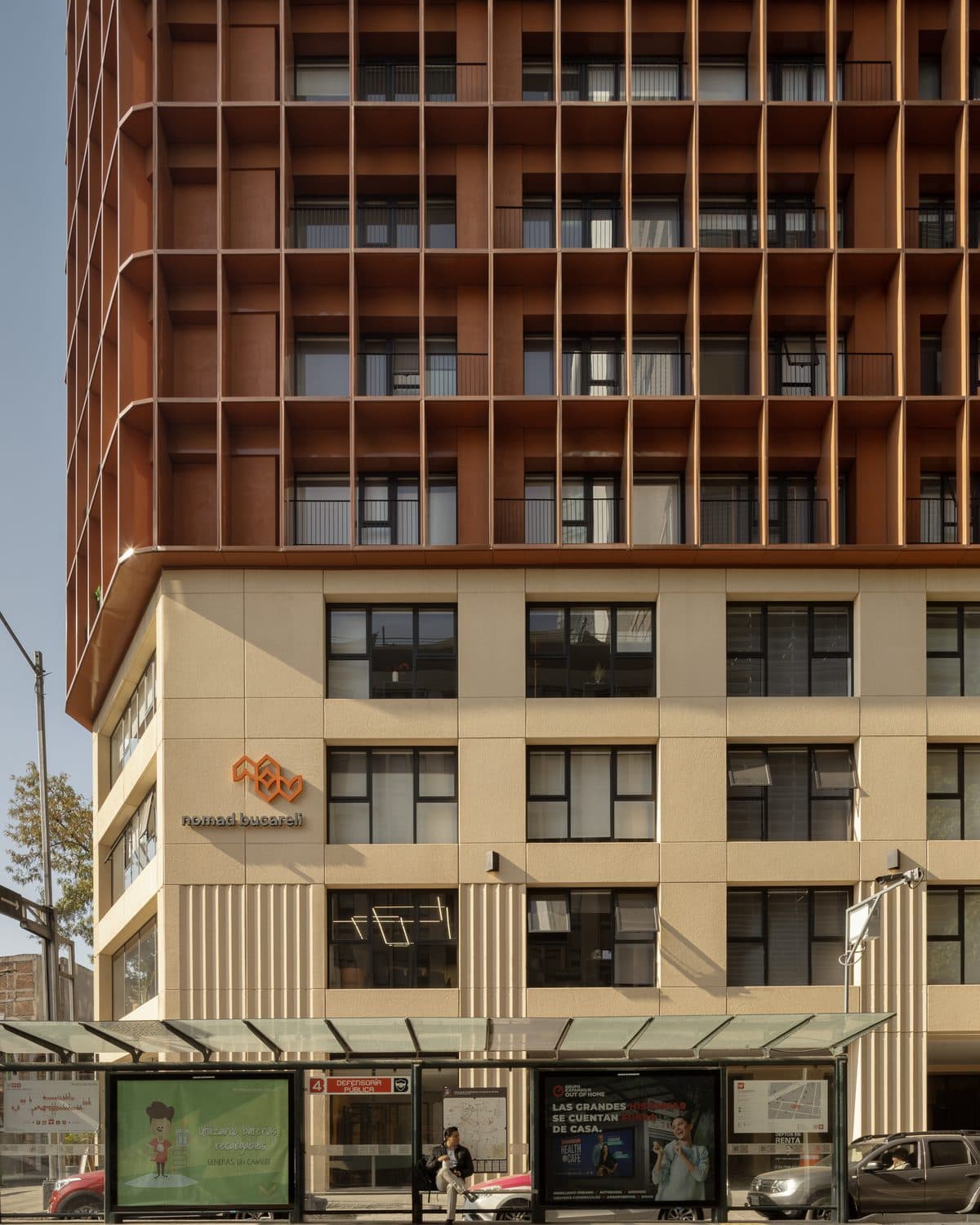 Nomad Bucareli, una torre de departamentos con celosía naranja sobre una base de piedra clara, vista desde la calle.